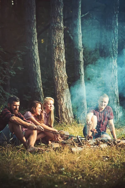 Piquenique na floresta de primavera. Caminhantes brindam salsichas na fogueira sentado no prado na floresta, viajar — Fotografia de Stock
