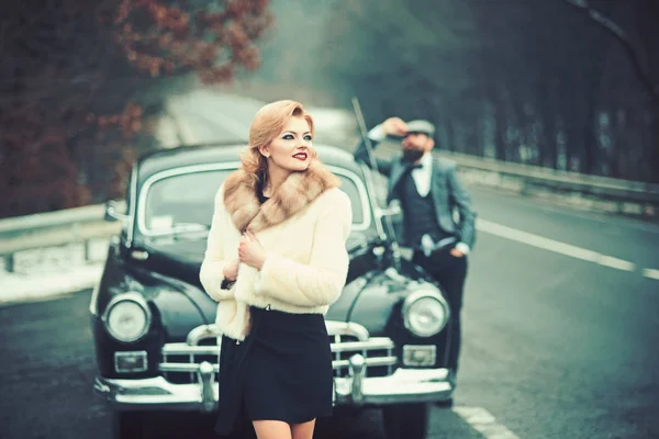 Viajes y viajes de negocios o autoestop. Coche de recogida retro y reparación de automóviles por conductor mecánico. Escolta de chica por seguridad. Hombre barbudo y mujer sexy en abrigo de piel. Pareja enamorada en una cita romántica . —  Fotos de Stock