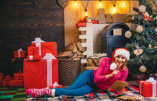 Sensuelle pour Noël. Blonde Santa femme tenant boîte cadeau au mur vintage. Femme en chapeau rouge Santa tenant présent. Portrait de mode de fille modèle à l'intérieur avec arbre de Noël. Santa femme posant . — Photo