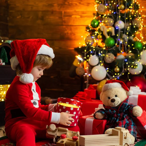 Criança feliz com caixa de presente de Natal. Um menino em roupas quentes sentado e brincando com brinquedos de madeira presente. Milagre de Natal e sentimentos de ano novo. Jogos Abertos. Primeira memória da infância . — Fotografia de Stock