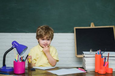 Ev veya okul eğitimi. İlkokuldan portre çocuğu. Mutlu sevimli çalışkan çocuk kapalı bir masada oturuyor - okul konsepti.
