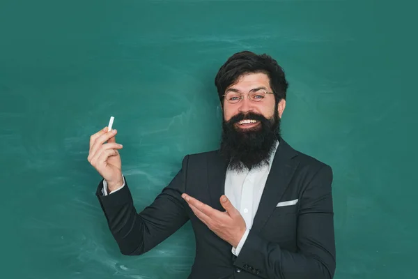 Student and tutoring education concept. School concept. Knowledge day. Young bearded teacher near chalkboard in school classroom. Back to school and happy time.