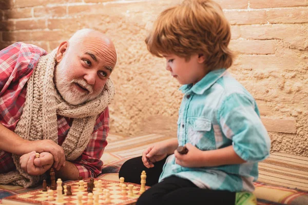 Ein älterer Mann denkt über seinen nächsten Zug in einer Schachpartie nach. Großvater und Enkel beim Schachspielen. Großvater spielt Schach mit seinem Enkel. — Stockfoto