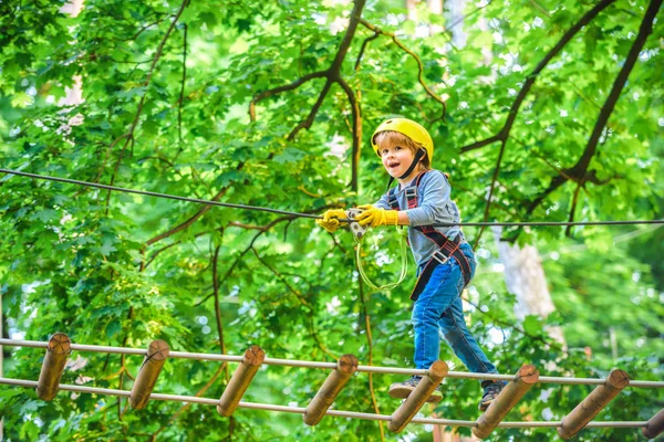 Παιδική αναρρίχηση σε ψηλό πάρκο με σχοινιά. Ευτυχισμένο παιδί που σκαρφαλώνει στα δέντρα. Το μικρό αγόρι απολαμβάνει τα παιδικά χρόνια. Πάρκο ροπινγκ — Φωτογραφία Αρχείου