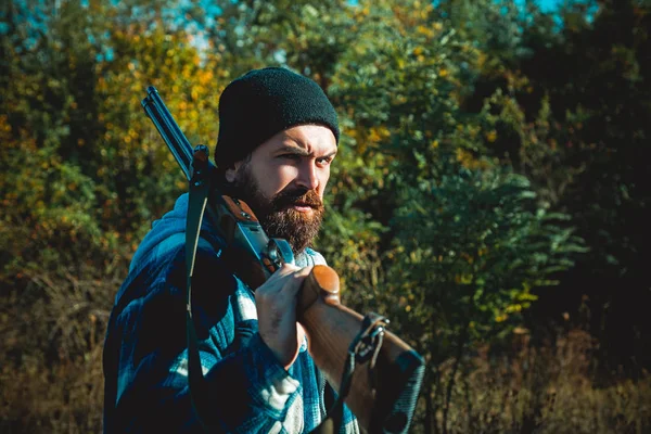 Silah tutan ve ormanda yürüyüş sakallı avcı adam. Hunter avı av tüfeği silah ile. — Stok fotoğraf