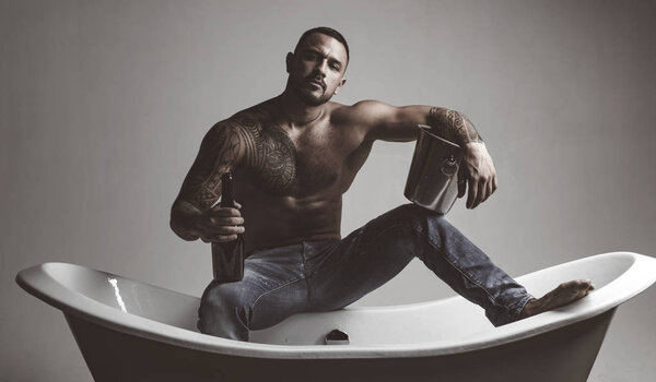 The best way to relax after a stressful workday. Atheltic hispanic man drinking champagne to relax. Strong latino man with tattoo on fit torso relax and enjoy in bath. Stress relieving spa relax