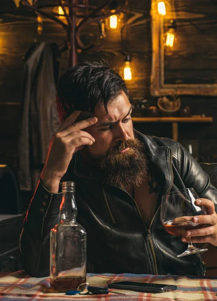 Drinking man. Man with beard holds glass brandy. Man holding a glass of whisky. Sipping whiskey. Degustation, tasting. Macho is drinking whiskey by his laptop.Thinking man.