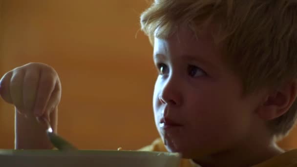 Éhes kisfiú eszik. Gyermekkori. Gyerek fiú eszik egészséges ételt otthon. Mosolygó boldog imádnivaló baba eszik gyümölcsöt cefre a konyhában. — Stock videók