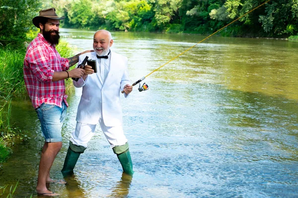 Happy father and son together fishing in summer day under beautiful sky on the river. Fly fishing for trout. Generations men. Brown trout fish. Royalty Free Stock Photos