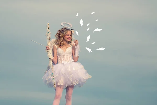 Uma criança na roupa de um anjo no fundo do céu. Miúda querubim. Conceito de criança inocente. Um belo adolescente com cabelo encaracolado loiro e um arco e flecha como cupido Dia dos Namorados. Menina inocente — Fotografia de Stock