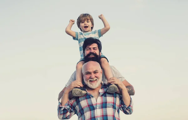 Aufgeregt. Vater und Sohn spielen im Freien. glücklich lächelnder Junge auf Schulter Papa schaut in die Kamera. glückliche Familie. Generation der drei Männer. — Stockfoto