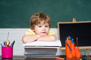 Okula dönüyoruz. Sevimli çalışkan çocuk kitap kapalı-okul konsepti ile bir masada oturuyor.