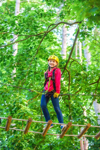 Beautiful little child climbing and having fun in adventure Park. Hiking in the rope park girl in safety equipment. Kid climbing trees in park. Cute child boy.