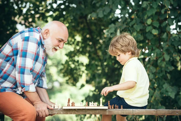 Abuelo y nieto jugando ajedrez. Abuelo y nieto están jugando ajedrez y sonriendo mientras pasan tiempo juntos en el parque . — Foto de Stock