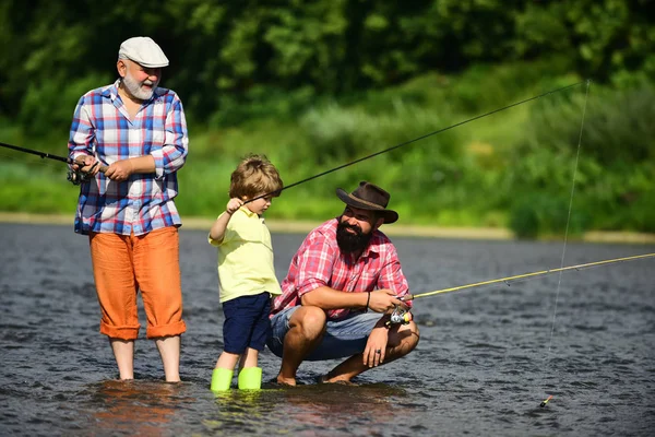 Un uomo che insegna ai bambini a pescare nel fiume. Padre, figlio e nonno che pescano. Generazioni uomini. Tre generazioni di età: nonno, padre e giovane figlio adolescente . — Foto Stock