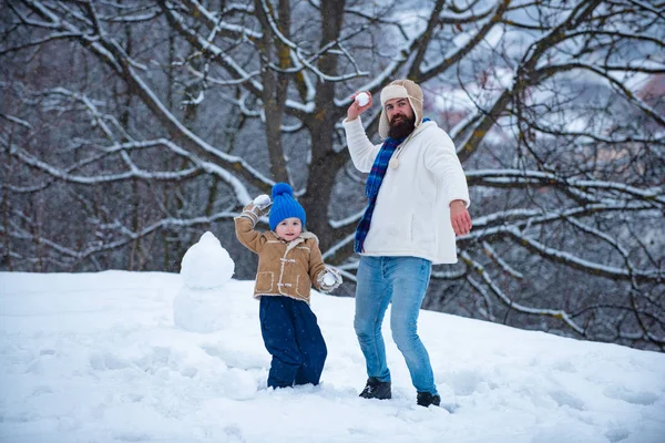 Padre e hijo juegan con bola de nieve sobre fondo blanco de invierno. Las fiestas navideñas y el invierno un nuevo año con el padre y el hijo. — Foto de Stock