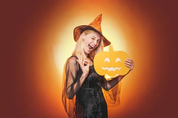 Uroda kobieta stwarzające z dyni i Halloween kapelusz. Zbliżenie portret wspaniały szczęśliwy blond bajki Zaklinacz, obejmujące jej oczy z kapelusza, gorąca figura, ciało. Dynia głowa Jack latarnia. — Zdjęcie stockowe