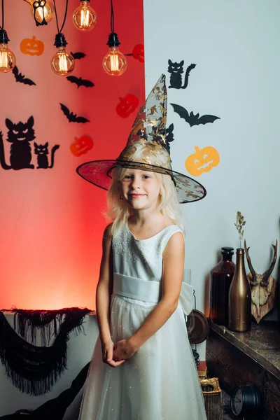 Schattige kleine heks met een pompoen. Mooie jonge verrast meisje in heksen hoed en kostuum houden pompoen. Halloween heks met pompoen. Gelukkig lachen Kid in kostuum aan Halloween. — Stockfoto