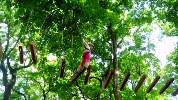 Actividades de verano para niños. Puentes de cuerda y viga de equilibrio. Retrato de un hermoso niño en un parque de cuerdas entre árboles. Red de carga de escalada y registro colgante. Parque de cuerdas . — Vídeo de stock