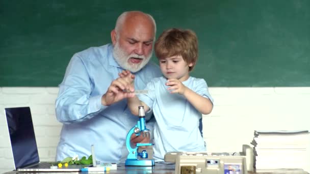 Friendly child boy with old mature teacher in classroom near blackboard desk. Grandfather and grandson. Grandfather and grandchild. Cute little preschool kid boy with Grandfather in a classroom. — Stock Video