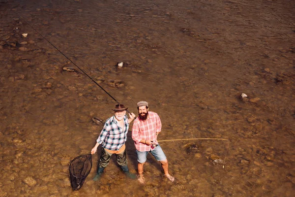 Uomini che pescano nel fiume durante la giornata estiva. La pesca divenne un'attività ricreativa popolare. Pescatore pesca con bobina di filatura. Pescatore a mosca sul fiume. Pesca a mosca . — Foto Stock