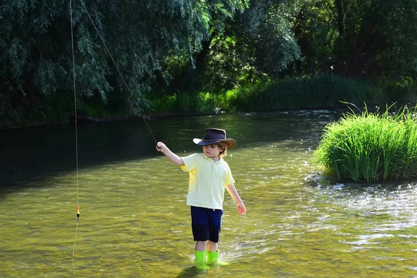 Bambini che pescano. Ragazzino tirando canna da pesca durante la pesca nel fine settimana. Pescatore col cappello. Ragazzo carino sta pescando nel fiume in estate . — Foto Stock