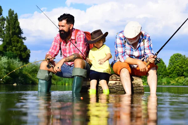 Ragazzo con padre e nonno pesca a mosca all'aperto sullo sfondo del fiume. Concetto giovane - adulto. Vecchi e giovani. Ragazzino su un lago con suo padre e suo nonno . — Foto Stock