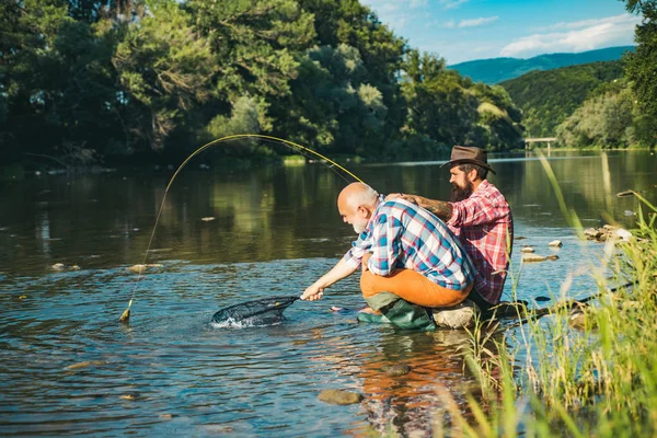 De visserij werd een populaire recreatieve activiteit. Visser en trofee forel. Vader en zoon vissen. Generaties mannen. Vissen in de rivier. — Stockfoto