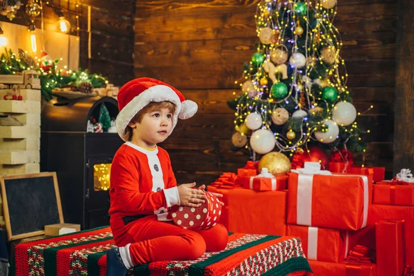 素敵な赤ちゃんはクリスマスをお楽しみください。サンタ少年の小さな子供は、自宅でクリスマスを祝います。家族の休日。男の子かわいい子供陽気な気分はクリスマスツリーの近くで遊びます。陽気で明るいクリスマスオープニングギフト — ストック写真
