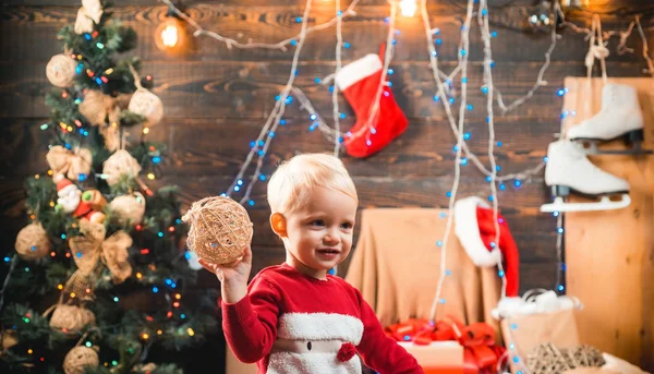 Winterabend zu Hause. Eröffnungsgeschenke zu Weihnachten und Neujahr. Ein fröhliches kleines Kind in Winterkleidung denkt an den Weihnachtsmann in der Nähe des Weihnachtsbaums. Kinderweihnachten. Weihnachtskinder. — Stockfoto