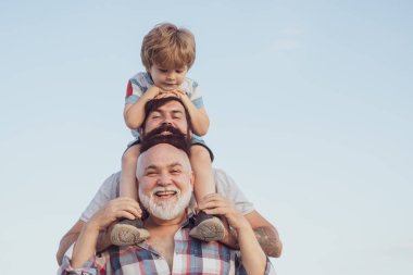 Babalar günün kutlu olsun. Baba ve oğul dışarıda eğleniyor. Erkek nesil: dedesi baba ve torunu kameraya bakarak ve gülümseyerek sarılma vardır.