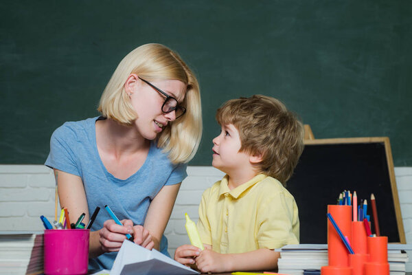 Home schooling or private school. Funny little child and young female teacher having fun on blackboard background.