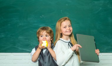 Yeşil tahtaya karşı okul çocukları. Kız ve erkek okul malzemeleri ile masa nın yanında mutlu yüz ifadesi ile. Öğretmen Schoolgirl okulda sınıfta ödevleri ile çocuklara yardım.