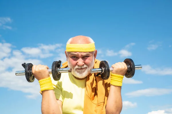 Velho desportista exercitando com haltere de elevação no fundo do céu azul. Isolado, espaço de cópia . — Fotografia de Stock