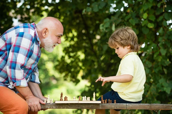 Opa und Enkel spielen Schach, während sie Zeit miteinander verbringen. Kleiner Junge spielt Schach mit seinem Großvater. — Stockfoto