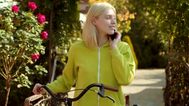 Ragazza felice posa con il telefono. Donna bionda in camicia verde gioire e tenere il telefono cellulare in mano . — Video Stock