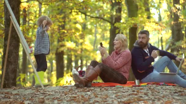 Happy Child artist ritning bild på höst natur. Lyckligt ungt par med manliga barn utomhus. Unga föräldrar och barn som har picknick och slappnar av tillsammans på en höst solig dag. — Stockvideo