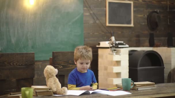 De volta à escola. Feliz desenho de pupila sorridente na mesa. Criança na sala de aula com quadro-negro no fundo. Urso de peluche, lápis, máquina de escrever, livros. Rapaz da escola primária. Primeiro dia de queda . — Vídeo de Stock