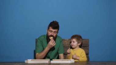 Sevimli küçük beyaz çocuk ve pizza yiyen adam. Aç çocuk pizzadan bir ısırık alıyor. Lezzetli yemekler. Pizzalı aile yemeği. Aile, mavi arka planda izole edilmiş pizza yer. Lezzetli yemekler. Erkekler yemek.