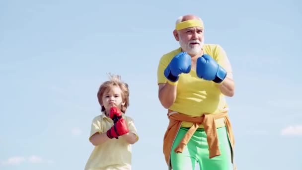 Combattant sain Grand-père et petit-fils avec des gants de boxe. Grand-père et petit-fils s'entraînent à la boxe le matin. Entraîneur senior et petit garçon portant des gants de boxe . — Video
