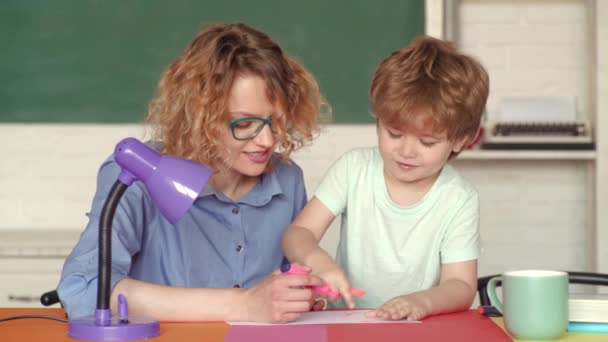 Genç anne oğlunun ev ödevi yapmasına yardım ediyor. Okul dışı çocuklar için eğitim. İlkokul öğrencisi kapalı alanda eğitim. — Stok video