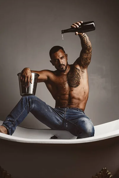 Luxury elite leisure. A concept of luxury life with champagne bottle. Brutal man with a bottle of champagne which pours into the bath. Luxury life. Attractive men with luxury elite alcohol.