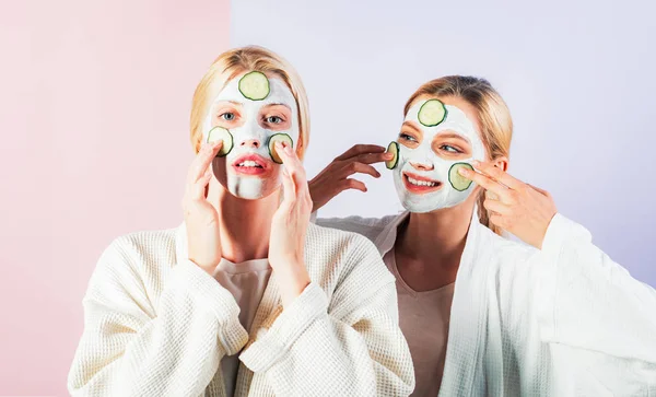 Concepción de cuidado de la piel mediante el uso de anillos de pepino fresco y máscara blanca en la cara. Dos hermanas tienen fin de semana en el dormitorio. — Foto de Stock
