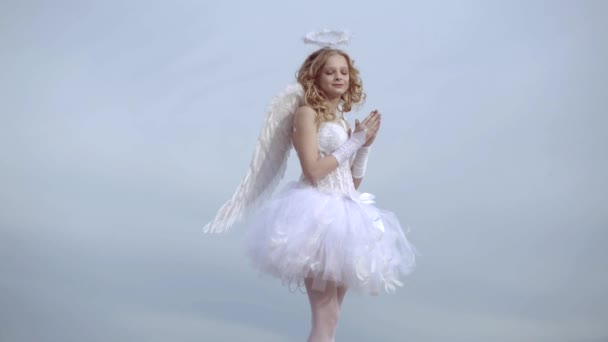 Chica ángel con halo en vestido de ángel blanco. Una hermosa adolescente con el pelo rubio rizado como Cupido - Día de San Valentín. Tarjeta de amor. Niña con alas de ángel y halo . — Vídeos de Stock