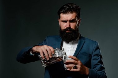 Barmen deri önlüğü bardakta viski kokteyli tutuyor. Sakallı ve bir bardak viski..