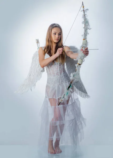 Encantadora mujer rizada en vestido blanco y alas - ángel chica Cupido. Personaje angelical. Feliz día de San Valentín - copia de espacio. Cupido lindo ángel con arco y flechas - Concepto de San Valentín Día. Tarjeta de amor . — Foto de Stock