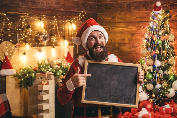 Hipster Weihnachtsmann mit Texttafel zu Hause. Frohes neues Jahr. bärtiger Mann im Weihnachtspullover. Frohe Winterzeit. Lustiger Weihnachtsmann. Weihnachtsvorbereitung - Mann feiert Neujahr. — Stockfoto