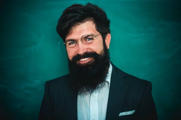 Teachers challenges and inspires. Bearded professor at school lesson at desks in classroom. Young bearded teacher near chalkboard in school classroom.