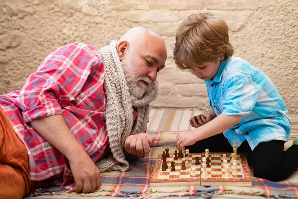 Opa und Enkel spielen Schach, während sie zu Hause Zeit miteinander verbringen. Kindheit. Konzept für Großvater und Enkel. — Stockfoto