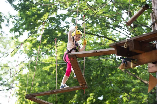 Enjoy childhood years. Happy little girl in summer. Playground. Cargo net climbing and hanging log. Cute school little girl enjoying a sunny day in a climbing adventure activity park.